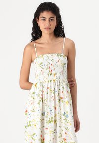 Λουλουδένιο φόρεμα με λευκό φόντο, διακοσμημένο με ραμμένο μπούστο, λεπτές τιράντες και φαρδιά φούστα με πολύχρωμα λουλούδια.