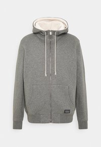 Grå zip-up hoodie med en mjuk krämfärgad fleecefoder, två framfickor, justerbara dragsnören och en tygetikett vid fållen.