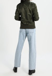 Zielona satynowa kurtka bomberka z prążkowanym kołnierzem i mankietami, w połączeniu z jasnoniebieskimi prostymi dżinsami i czarnymi masywnymi botkami.