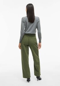 Maglione grigio a maniche lunghe abbinato a pantaloni larghi verdi a vita alta. I pantaloni presentano grandi tasche posteriori e una texture liscia.