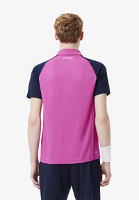 Lacoste kortärmad polo skjorta i rosa med marinblå raglanärmar, med en logotyp på ryggen och fukttransporterande tyg.