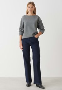 Grauer Sweatshirt mit geripptem Kragen und hochgekrempelten Ärmeln, kombiniert mit dunkelblauen Schlagjeans. Das Model trägt schwarze Absatzstiefel.