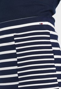 Marinblå och vit randig tyg med ribbad textur. Har en liten logotyp i rött och blått vid sömmen. Mjuk, elastisk material.