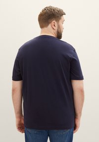 Granatowa koszulka z okrągłym dekoltem, z krótkimi rękawami, wykonana z gładkiej bawełnianej tkaniny, z prostym dołem i luźnym krojem.