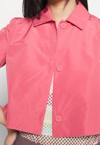 Roze, cropped jasje van lichtgewicht stof met een puntige kraag en afgeronde, decoratieve knopen. Daaronder een top met patroon.