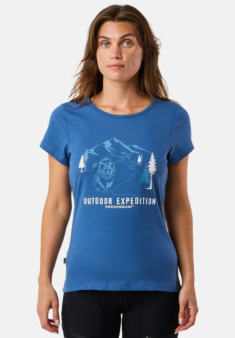 Donna che indossa una maglietta blu con una grafica di montagna, orso e alberi e il testo "Outdoor Expedition Swedemount."