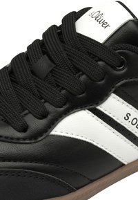 Sneaker in pelle nera con accenti bianchi e lacci neri. Presenta una superficie testurizzata e una suola in gomma marrone. Logo del marchio visibile.