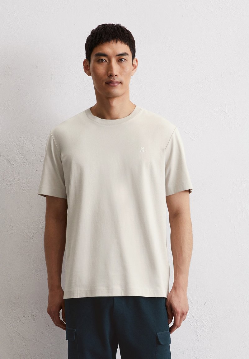 Lichtbeige T-shirt met korte mouwen van zachte katoen, voorzien van een klein logo op de borst, gecombineerd met donkerblauwe pantalons.