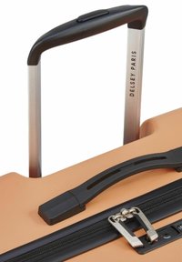 Valigia rigida arancione con superficie testurizzata, cerniera nera e manico doppio in alluminio. Marchio "Delsey Paris" presente sul manico.