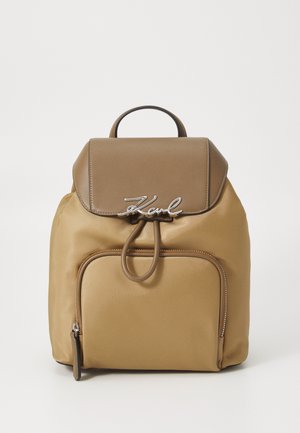 Brązowy plecak nylonowy o gładkiej teksturze, skórzanym klapie, srebrnym logo, z zamknięciem na sznurek i przednią kieszenią na zamek.