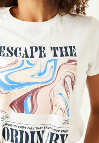 Camiseta de algodón blanca con un diseño mármole colorido que presenta remolinos en azul, rosa y marrón. El texto dice "ESCAPAR DE LO ORDINARIO".