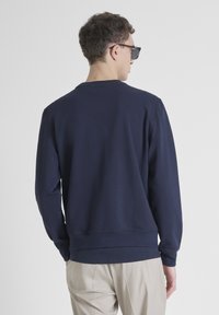 Sudadera de color navy con cuello redondo, mangas largas, puños y dobladillo acanalados, textura suave, y presenta un pequeño logo de la marca en la parte trasera del cuello.