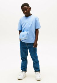 Lichtblauw t-shirt, blauwe schoudertas, blauwe denim jeans en witte sneakers. Het t-shirt heeft een klein logo op de borst.