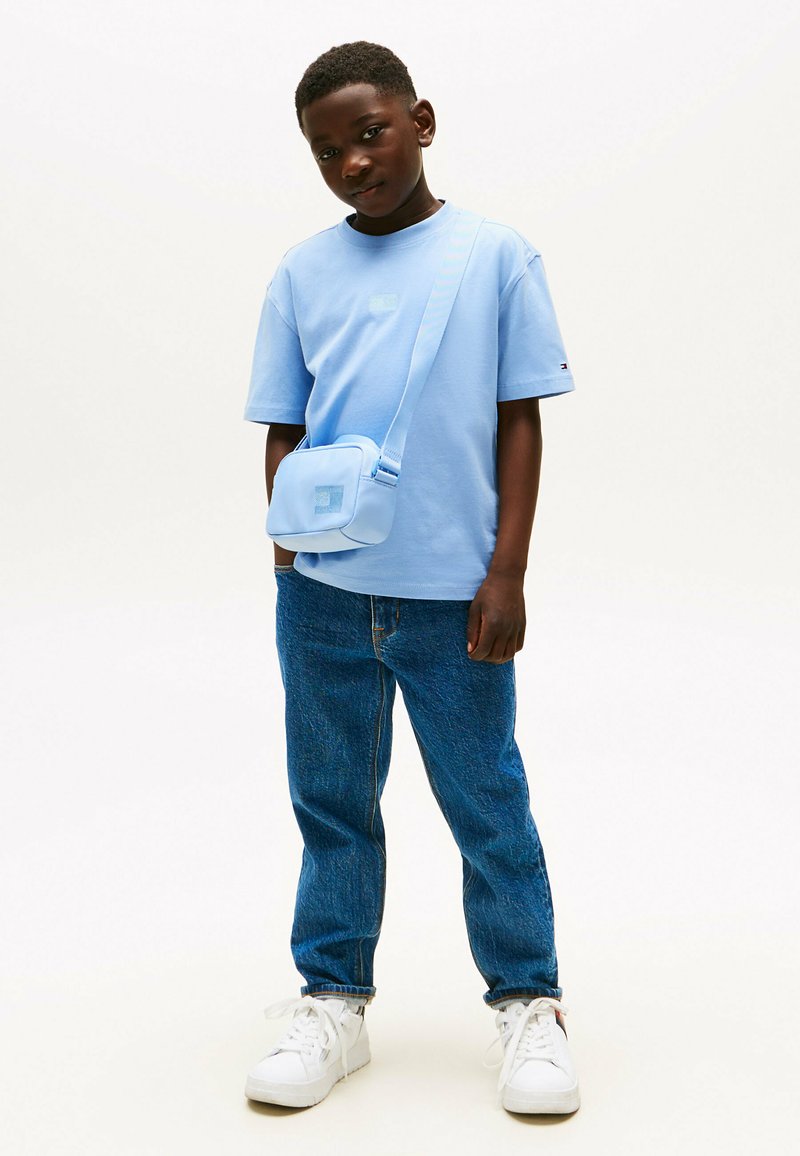 Lichtblauw t-shirt, blauwe schoudertas, blauwe denim jeans en witte sneakers. Het t-shirt heeft een klein logo op de borst.