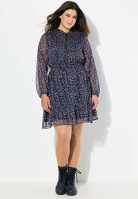 Navyblaues Kleid mit langen durchsichtigen Ärmeln, geraffter Taille und floralen Muster in Hellrosa. Kombiniert mit schwarzen Schnür-Stiefeletten.