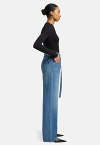 Jeans a gamba larga in denim blu con vita alta, passanti per la cintura e tasche laterali, abbinati a un top fitted nero a maniche lunghe.