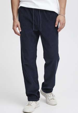 Navy corduroy pants with a relaxed fit, featuring a drawstring waist and vertical stripes. Paired with white sneakers.
