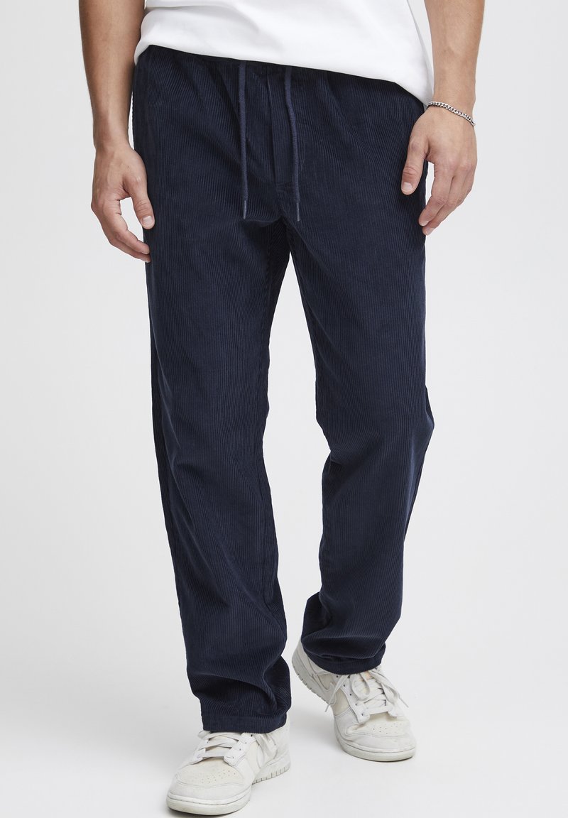 Navy corduroy pants with a relaxed fit, featuring a drawstring waist and vertical stripes. Paired with white sneakers.