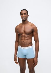 Světle modré boxerky s bílým pasem nesoucím logo "TOMMY HILFIGER". Hladká látka, přiléhavý střih, minimalistický styl.