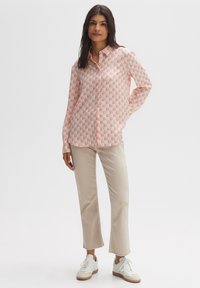 Long-sleeve shirt in light pink with a geometric pattern, button-down design, paired with beige cropped pants and white sneakers.