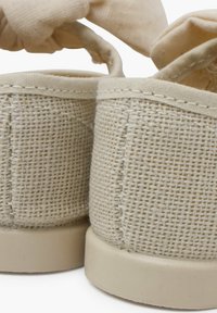 Zapatos de tela beige con un tejido texturizado, punta redondeada y una correa de tela suave. Suela de goma con un acabado liso, que muestra detalles de costura.