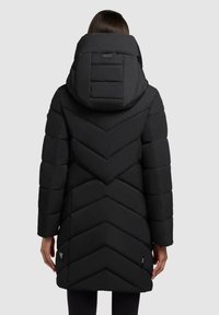Svart puffjacka med ett Chevron-mönster, stor huva och långa ärmar. Tillverkad av vadderat material, har en minimalistisk design och etiketter.