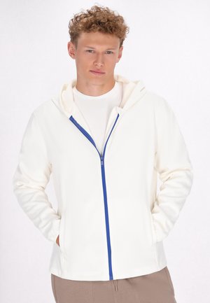 Witte hoodie met een blauwe rits, voorzien van een zachte binnenvoering en een voortasje. Model draagt een wit shirt eronder.