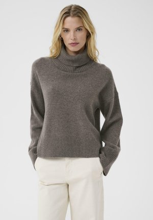 Brown knit turtleneck sweater with ribbed cuffs and hem. Soft texture, relaxed fit, and dropped shoulders. Paired with light beige pants.