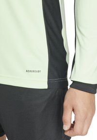 Lichtgroen sportshirt met lange mouwen en zwarte accenten, voorzien van het "AEROREADY" logo, contrasterende texturen en platte naden.