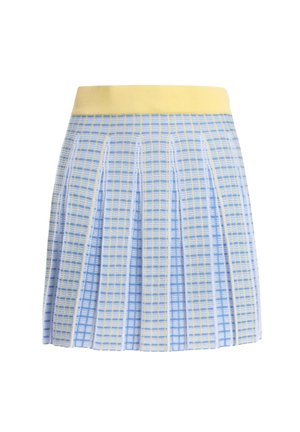 Gestrickter Rock mit blauem, weißem und gelbem Karomuster, breitem gelbem Bund, getragen von einer Person mit verschränkten Armen vor der Brust.