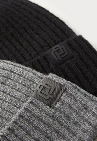 Două căciuli tricotate: una neagră, una gri deschis. Ambele au o textură în dungi și un patch pătrat negru cu logo pe lateral.