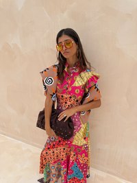 Kleurvolle jurk met gemengde patronen in roze, oranje, groen en bruin. Bevat een oversized mouw en een donkerbruin handtas met kleurrijke accenten.