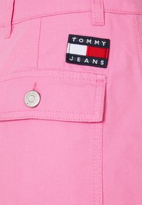 Jeans de mezclilla rosa que presentan un diseño clásico, un bolsillo de parche en la parte frontal y una etiqueta de Tommy Jeans con acentos en azul marino, rojo y blanco.