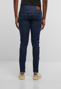 Jeans de color azul oscuro con un corte ajustado, diseño de cinco bolsillos y una etiqueta de cuero en la cintura, con detalles de costura sutiles.