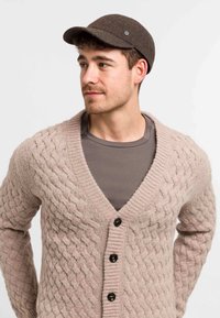 Light beige knitted cardigan with a textured cable pattern, button front, and deep V-neck design, paired with a brown herringbone cap.