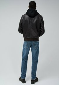 Bruine leren bomberjack met een zwarte hoodie eronder, gecombineerd met klassieke blauwe jeans en zwarte laarzen, gezien vanuit de achterkant.