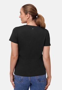 Svart bomulls t-shirt med rund halsringning, korta ärmar och en liten logotyp nära baksidan av kragen. Står i kombination med blå denimjeans.
