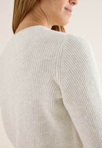 Hellgrauer, gerippter Strickpullover mit einem runden Halsausschnitt und taillierter Silhouette. Die Textur ist weich und leicht kuschelig, was den Stoff betont.