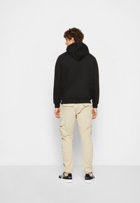 Svart hettegenser, beige cargo-bukser med lommer, brukt med svart og hvit sneakers. Enkelt design, uformelt utseende.