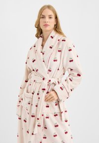 Albornoz de forro polar en rosa pálido con estampado de cerezas. Cuenta con cuello chal, cinturón de lazo y dos bolsillos delanteros. Textura suave con detalles de ribete rojo.
