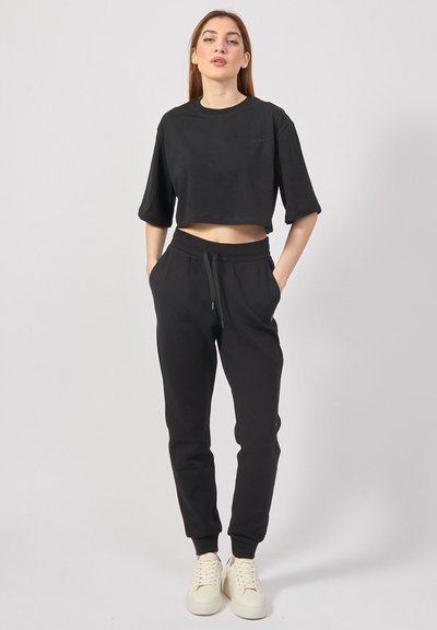 T-shirt nera cropped con maniche corte e dettaglio del logo, abbinata a pantaloni della tuta neri con vita elastica e polsini.
