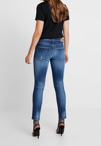 Úzké džínsy ve středně modré denimové barvě s vybledlým detailem, spárované s černým tričkem. Obuty s černými vysokými podpatky a rybářskými punčochami.