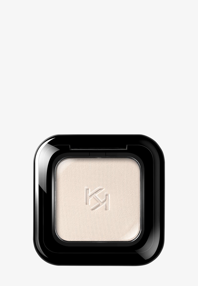 Ombre à paupières beige compacte carrée avec le logo "KM" en relief, encastrée dans un emballage en plastique noir brillant sur fond blanc.