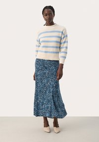 Pull tricoté rayé crème et bleu associé à une longue jupe fleurie bleue. Le mannequin porte des chaussures à talons beiges. Coupe et design simples et décontractés.