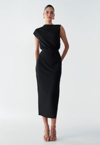 Abito midi nero con scollatura drappeggiata, vita elastica e texture sottile. Abbinato a sandali dorati con cinghie.