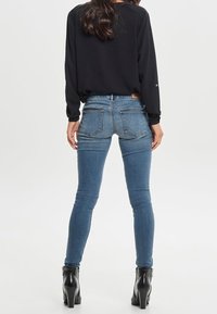 Maglietta nera a maniche lunghe abbinata a jeans skinny azzurri chiari, con tasche posteriori e una morbida trama in denim, indossata con stivali neri con tacco.