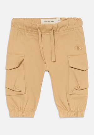 Pantalons cargo beiges avec une taille élastique, un cordon de serrage et des poignets côtelés. Comprend deux poches latérales et un logo Calvin Klein brodé.