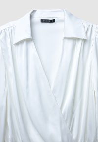 Blusa in satin bianco con colletto, design avvolgente e pieghe sottili. L'etichetta recita "CALLIOPE" in nero all'interno. Taglia "S."
