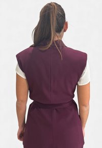 Gilet senza maniche color marrone scuro con colletto alto e cintura da annodare in vita. Presenta una trama liscia e una vestibilità sartoriale, visto da dietro.