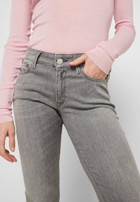 Grey denim jeans with a straight fit, five-pocket design, and a metal button closure. Paired with a long-sleeve light pink top.